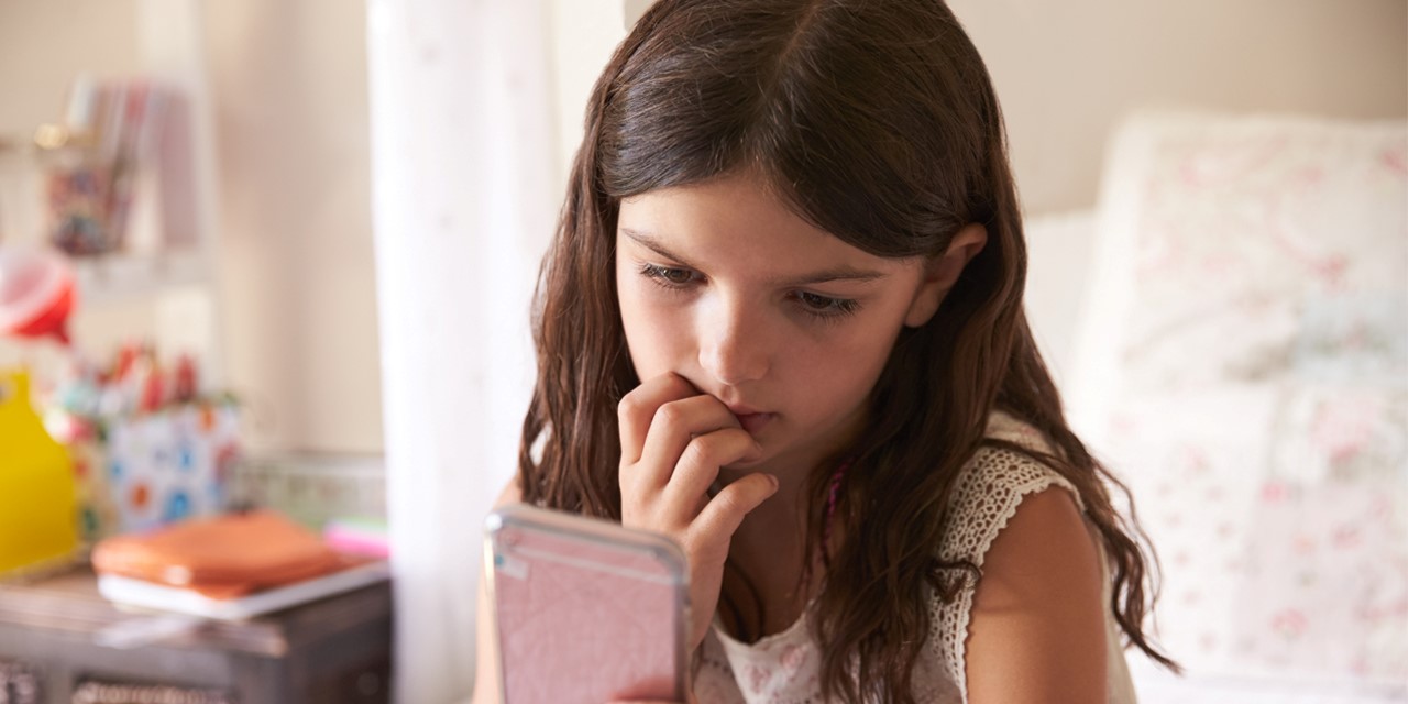 A child views her mobile phone with a worried expression